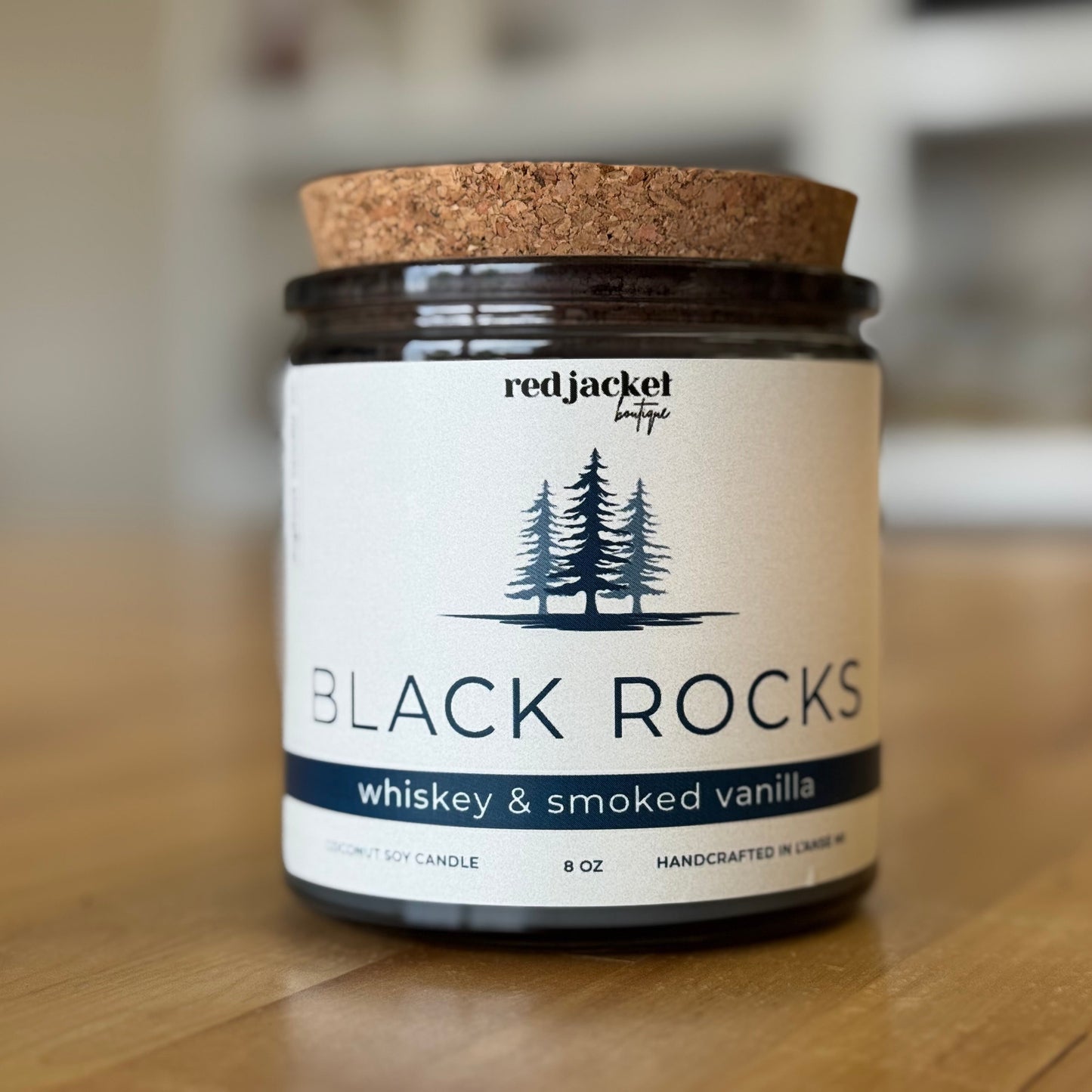Candle jar labeled 'Black Rocks' by Red Jacket Boutique on a wooden surface.