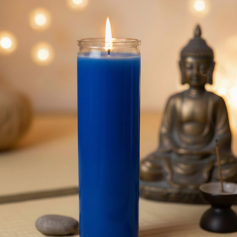 
                  
                    A tall, dark gray pillar candle in a clear glass jar, lit with a small flame, set on a woven mat with spa stones and a bronze Buddha statue in the background.
                  
                