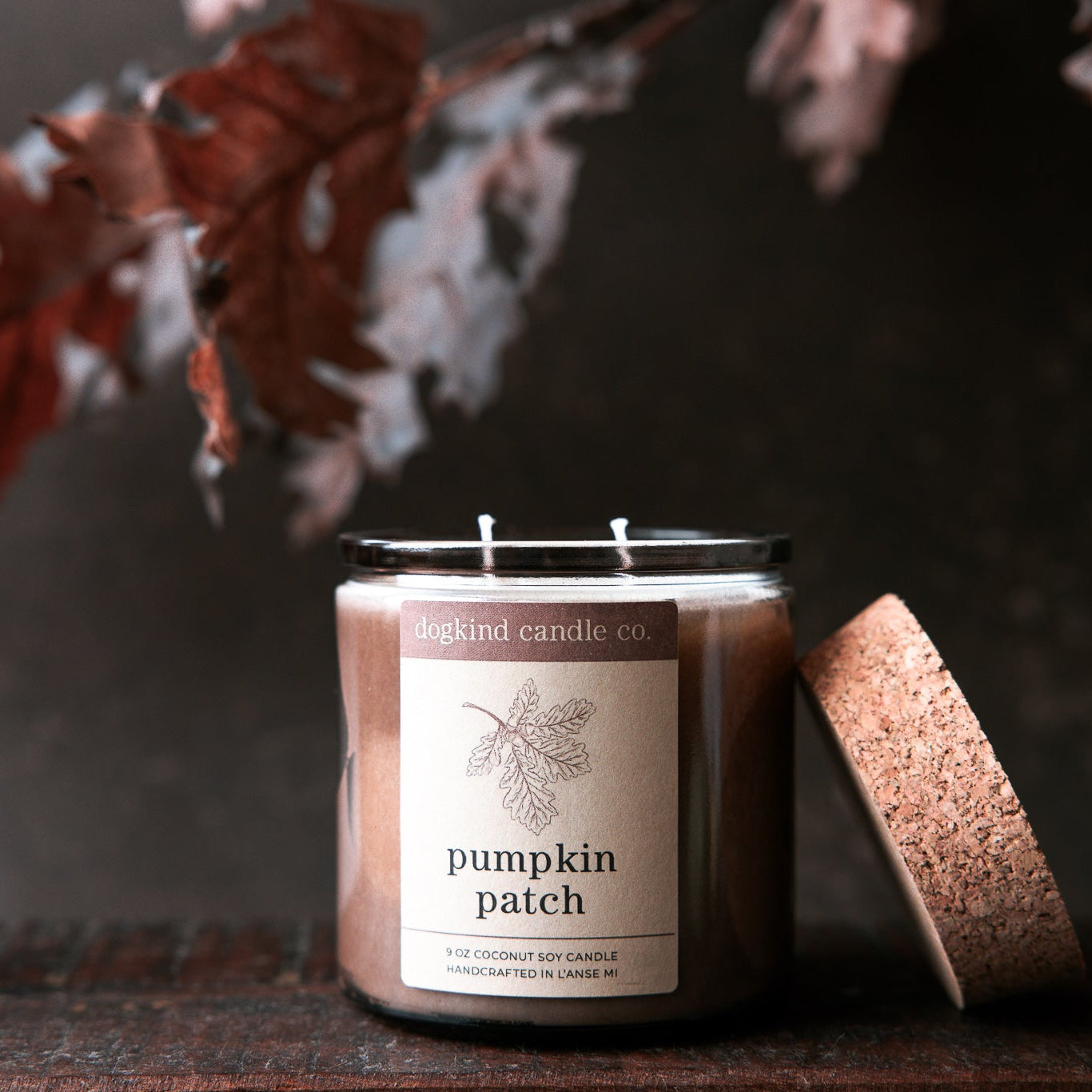 Fall scented Candle labeled 'Pumpkin Patch' with a cork lid on a dark background with autumn oak leaves.