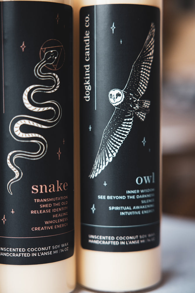 Two candles with snake and owl designs on black labels, featuring text about their spiritual meanings.