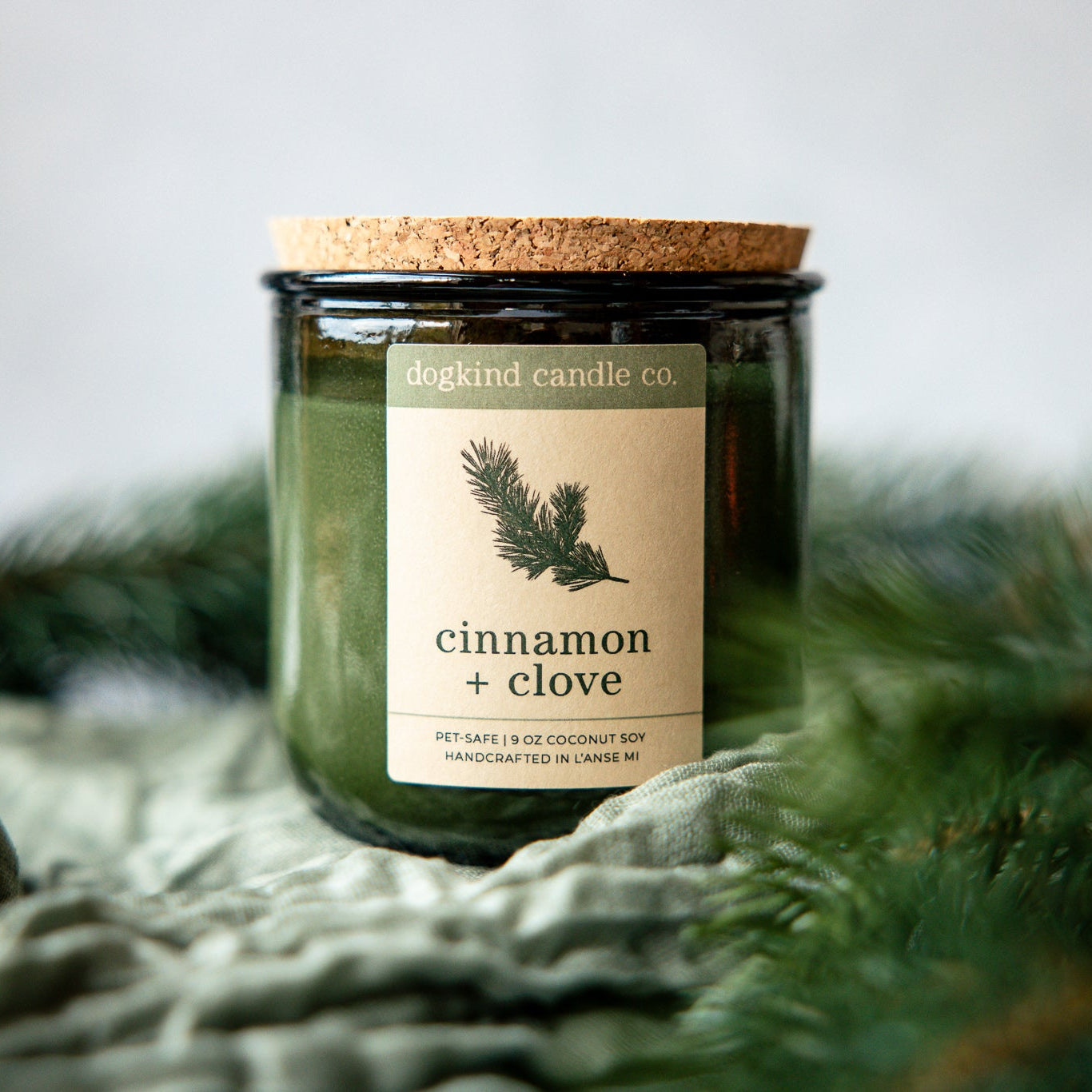 Cinnamon + Clove  holiday candle from Dogkind Candle Co. on a textured surface with pine greenery in the background.