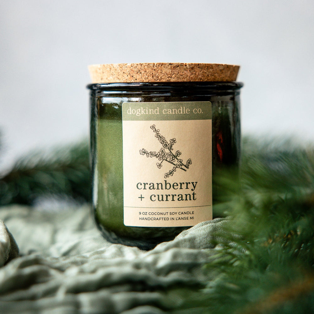 Cranberry Currant  holiday candle from Dogkind Candle Co. on a textured surface with pine greenery in the background.