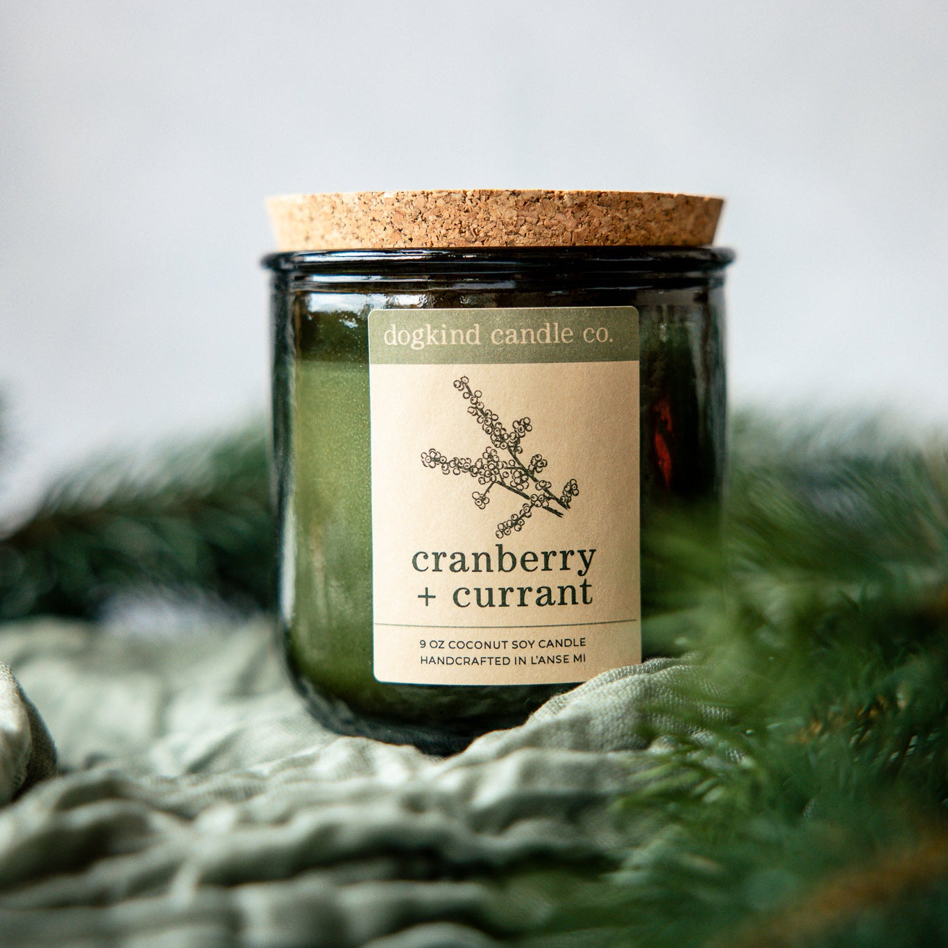 Cranberry Currant  holiday candle from Dogkind Candle Co. on a textured surface with pine greenery in the background.