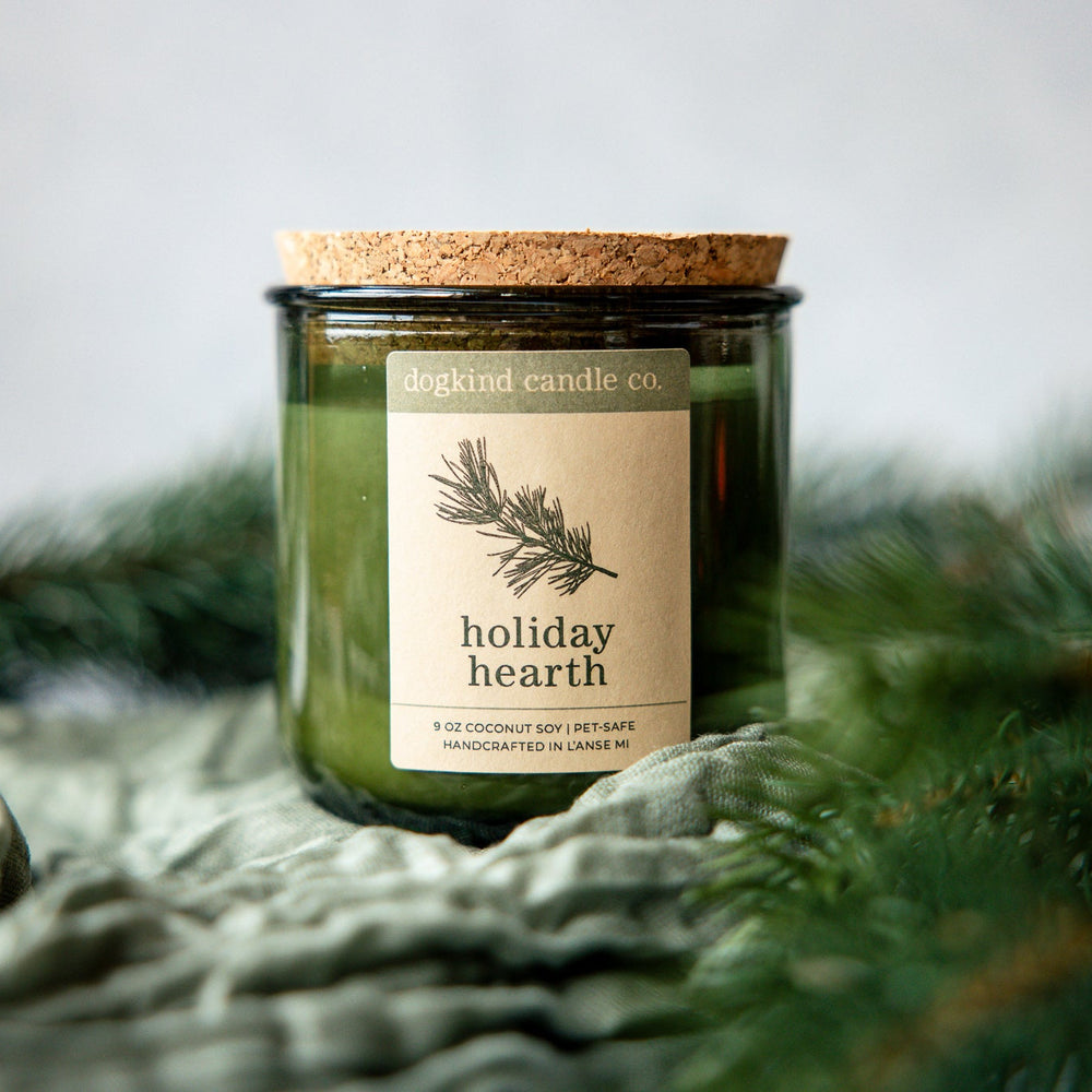 Holiday Hearth  holiday candle from Dogkind Candle Co. on a textured surface with pine greenery in the background.