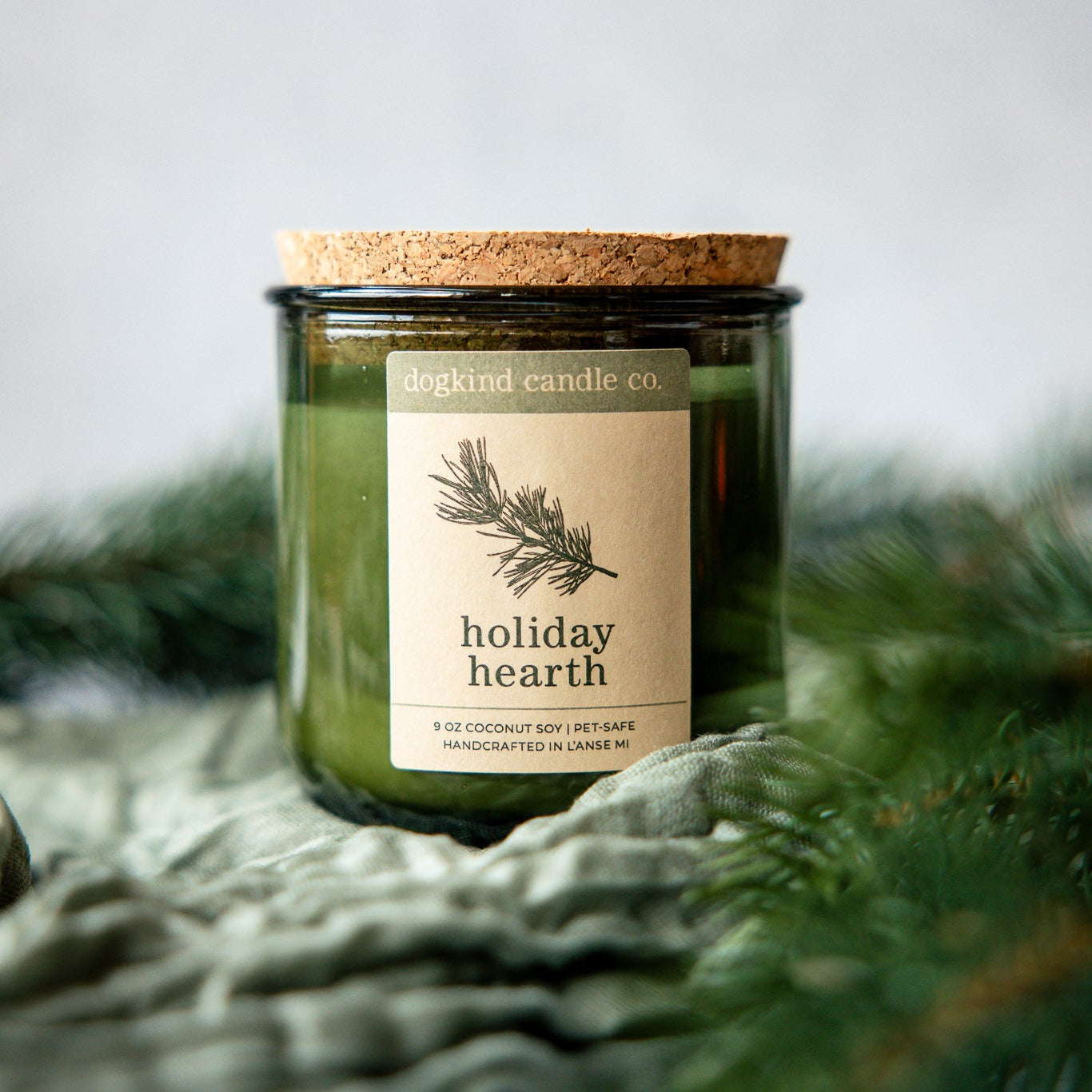 Holiday Hearth  holiday candle from Dogkind Candle Co. on a textured surface with pine greenery in the background.