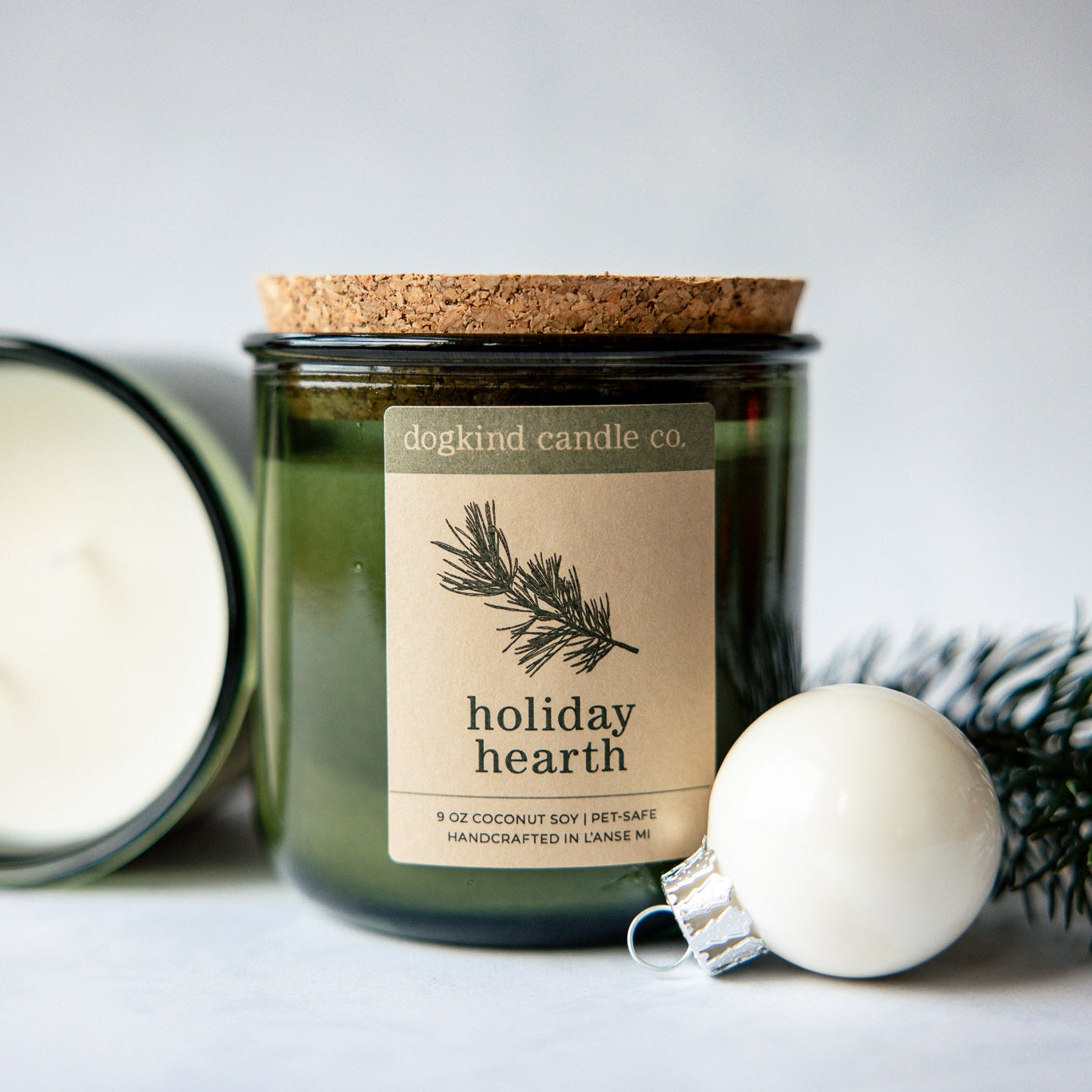 
                  
                    Holiday Hearth  holiday scented candle from Dogkind Candle Co. on a textured surface with pine greenery and Christmas ornament in the background.
                  
                