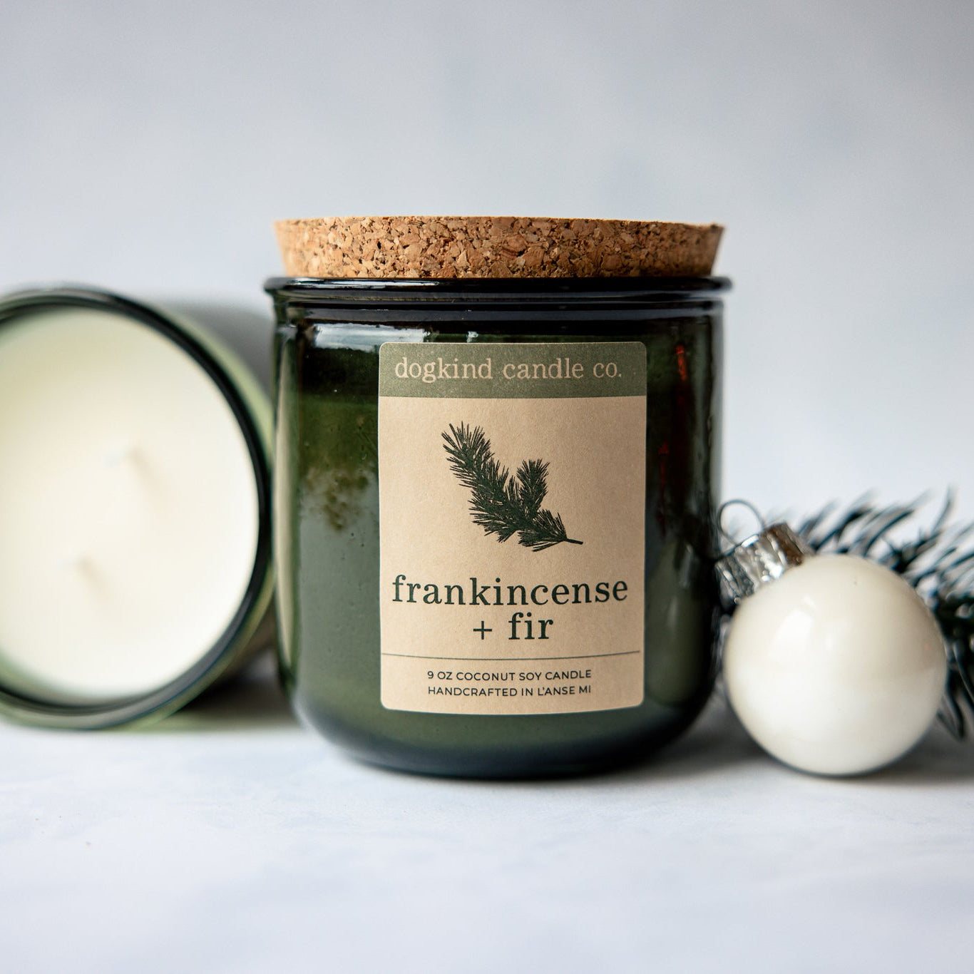 
                  
                    Frankincense + Fir  holiday candle from Dogkind Candle Co. on a textured surface with pine greenery and Christmas ornament in the background.
                  
                