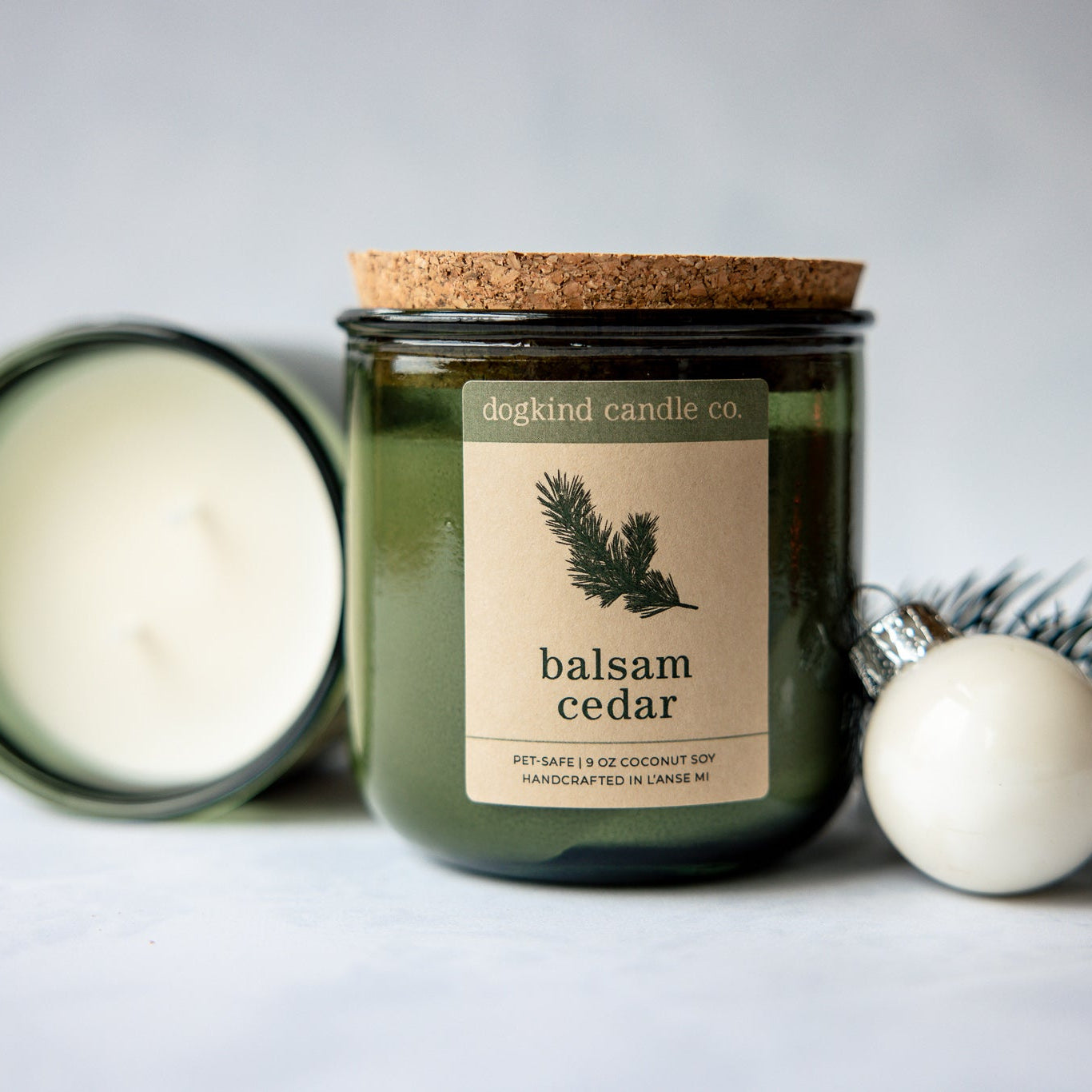 
                  
                    Balsam Cedar holiday candle from Dogkind Candle Co. on a textured surface with pine greenery and Christmas decorations in the background.
                  
                