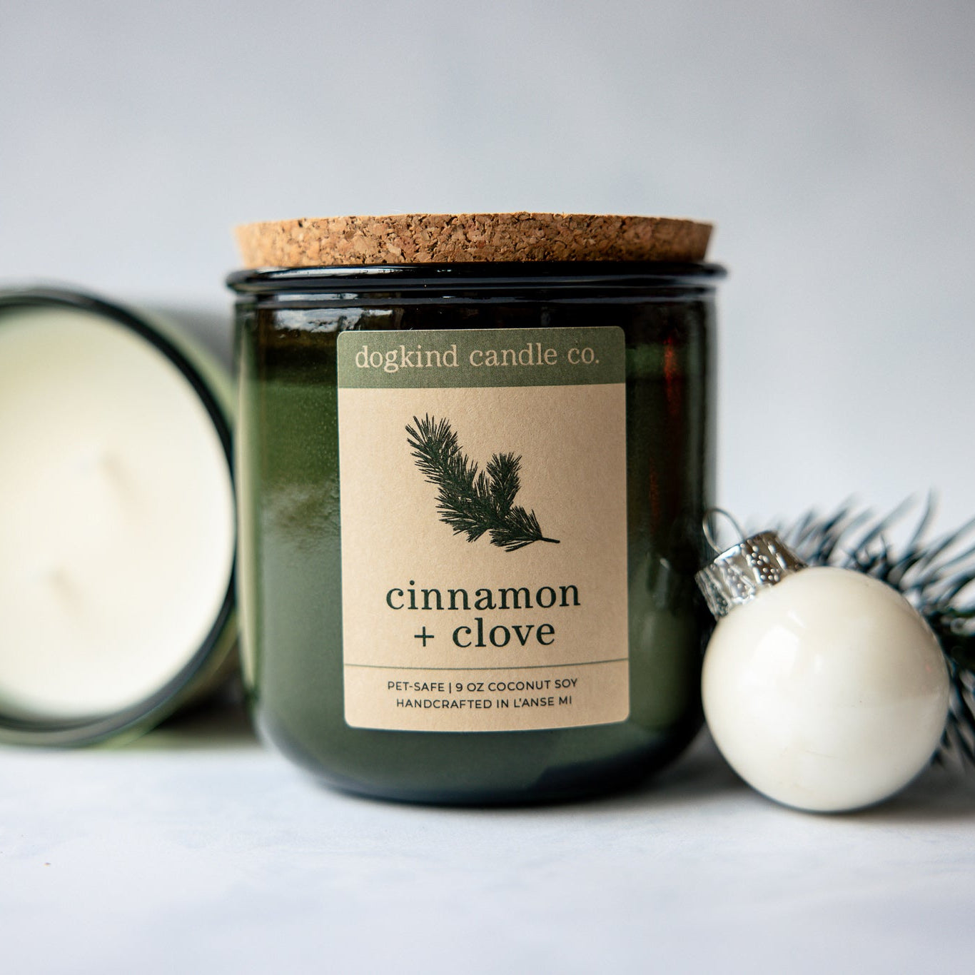 Cinnamon + Clove  holiday candle from Dogkind Candle Co. on a textured surface with pine greenery and Christmas ornament in the background.
