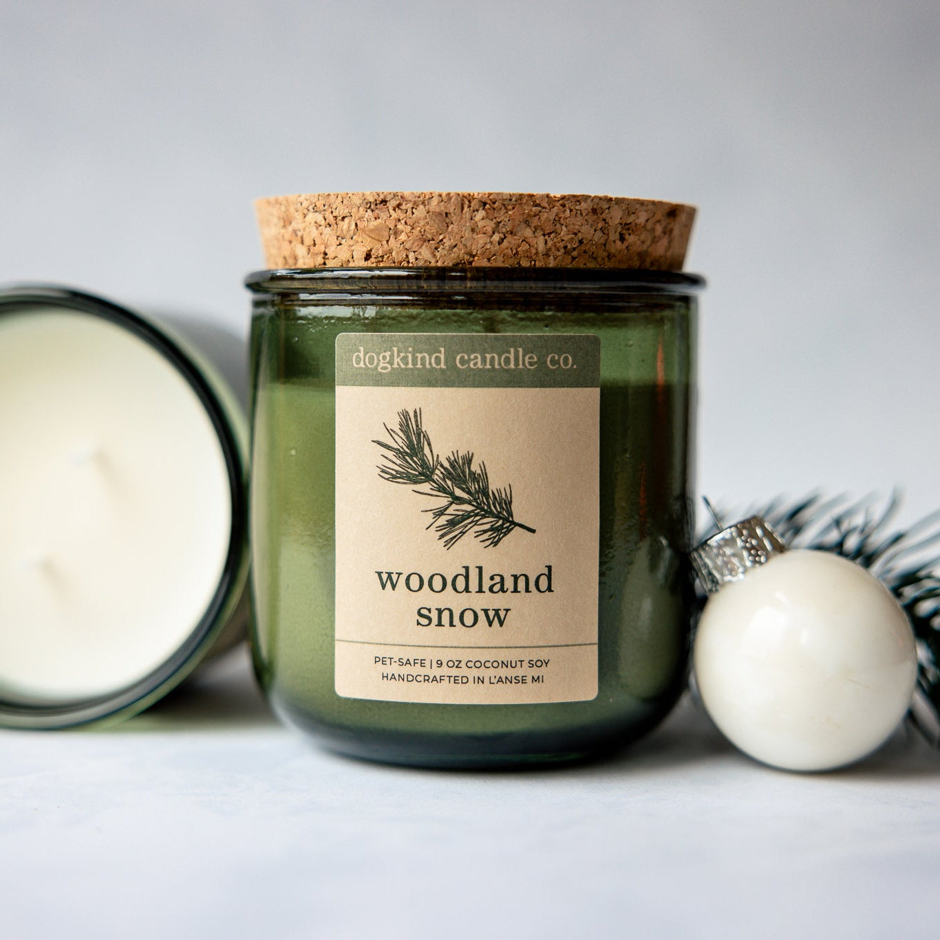 
                  
                    Woodland Snow holiday scented candle from Dogkind Candle Co. on a textured surface with pine greenery and Christmas ornament in the background.
                  
                