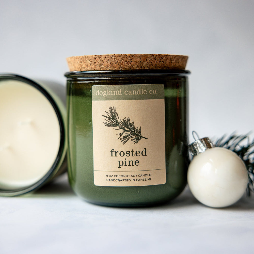 
                  
                    Frosted Pine  holiday candle from Dogkind Candle Co. on a textured surface with pine greenery and Christmas ornament in the background.
                  
                