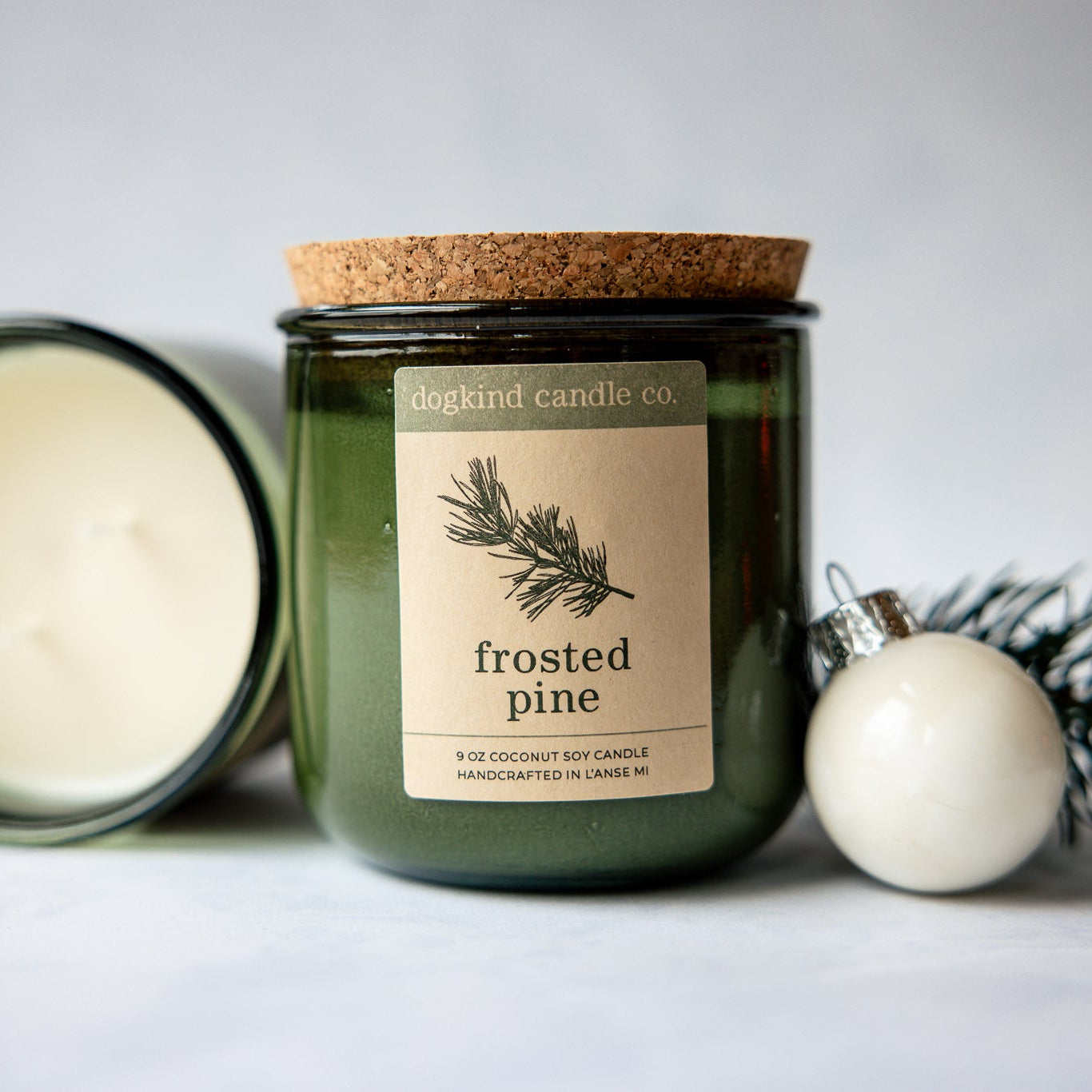 
                  
                    Frosted Pine  holiday candle from Dogkind Candle Co. on a textured surface with pine greenery and Christmas ornament in the background.
                  
                