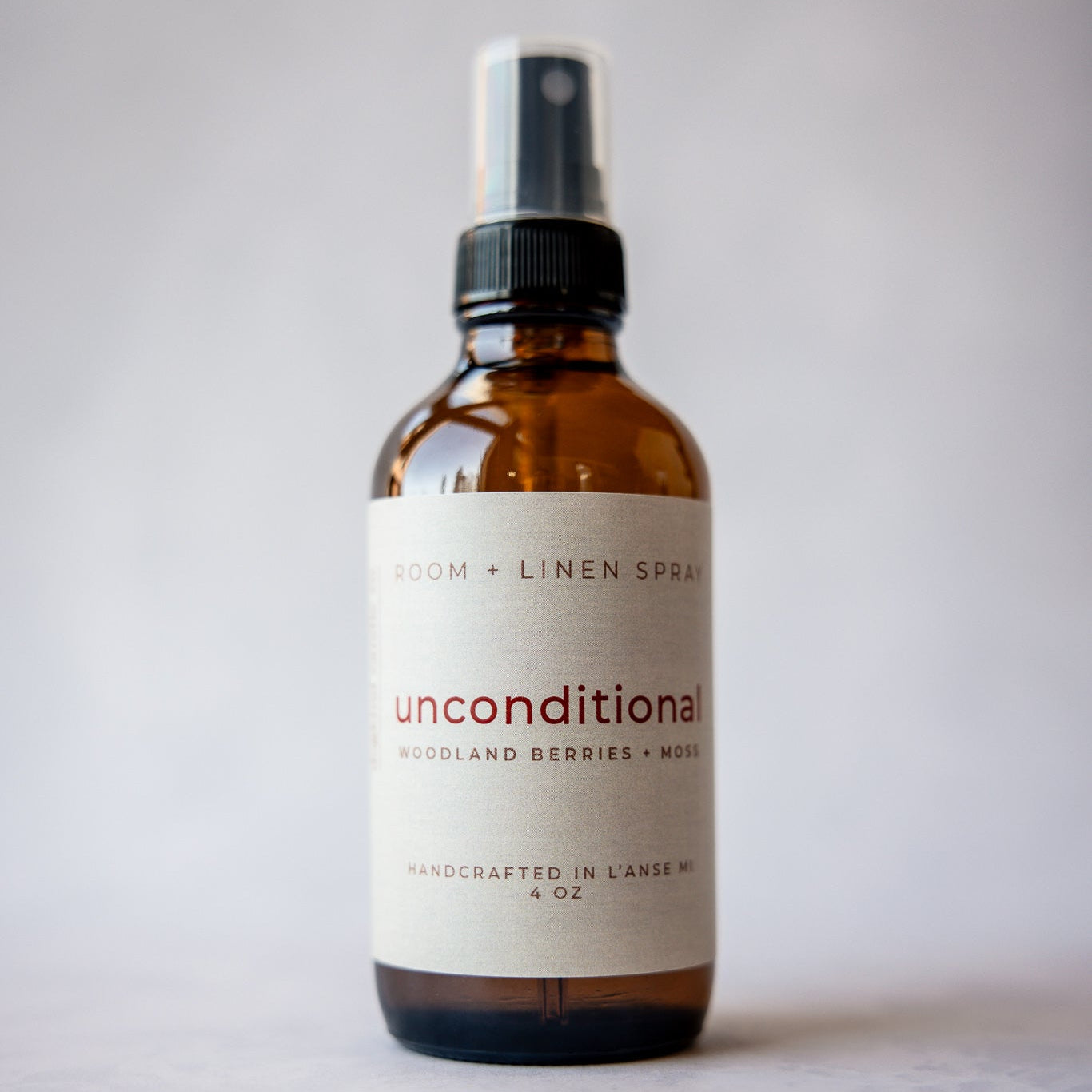 Brown room and linen spray bottle labeled 'unconditional' on a light gray background