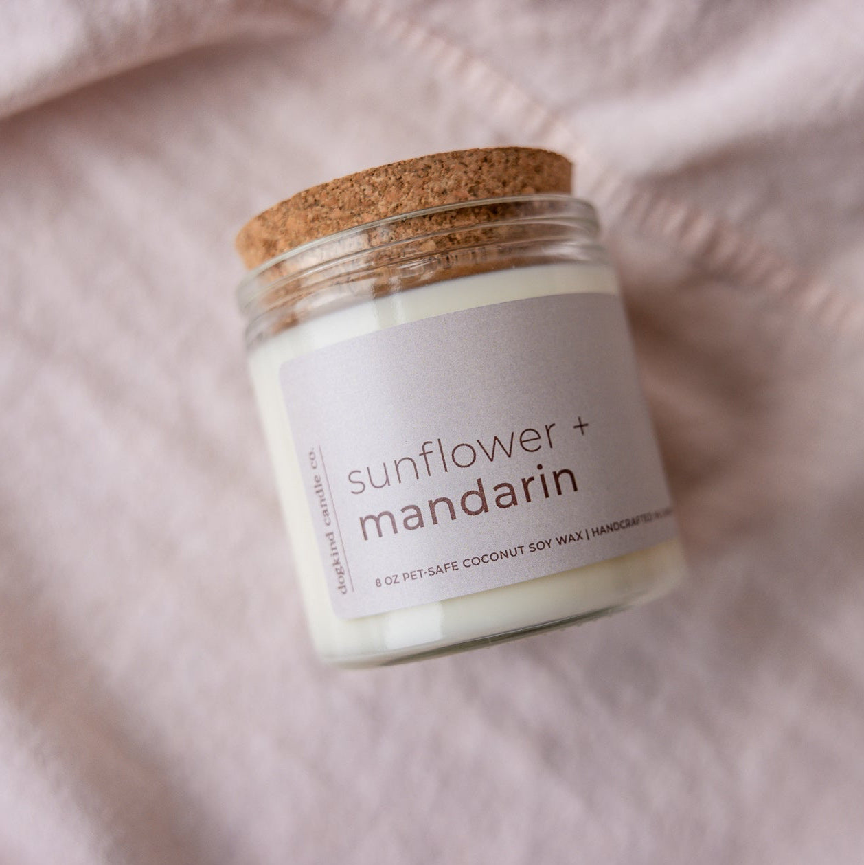 
                  
                    Candle jar labeled 'sunflower + mandarin' on a soft pink fabric background
                  
                