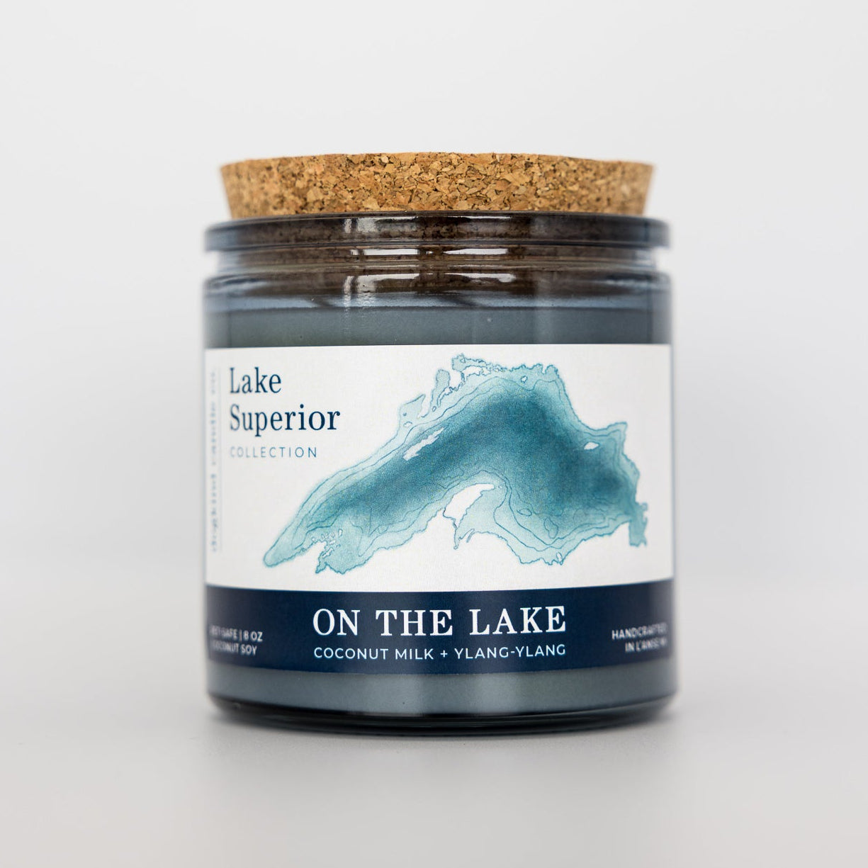 Candle jar with cork lid and 'On the Lake' label on a light gray background