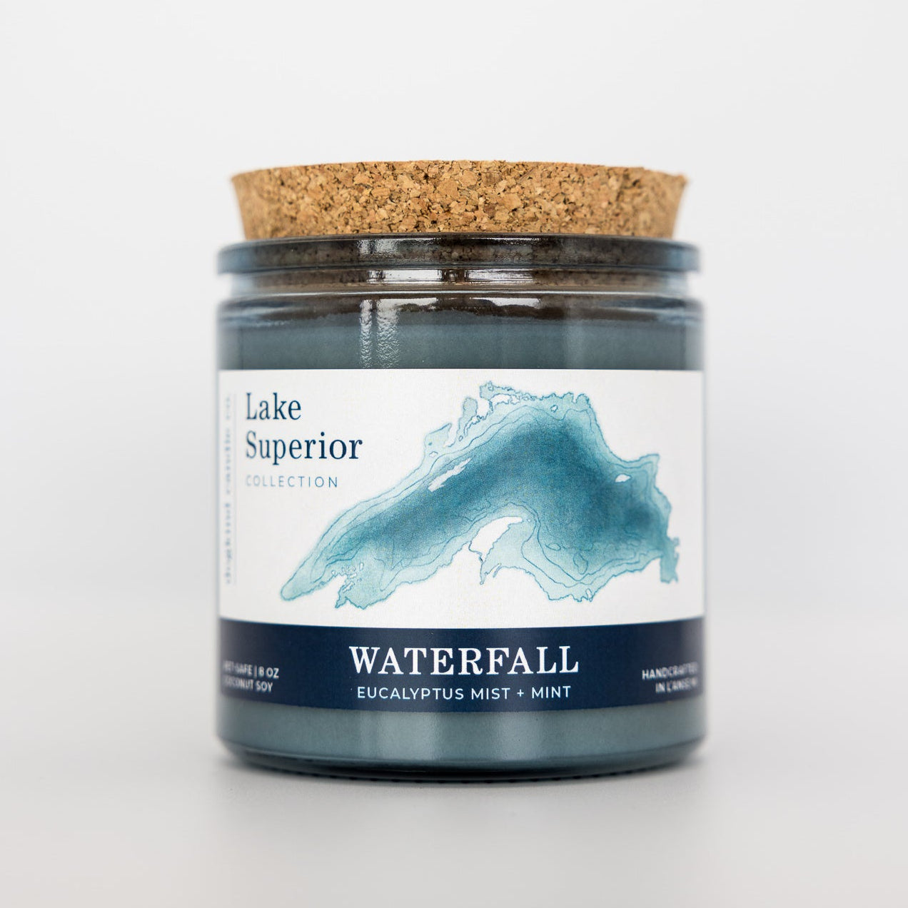Candle jar labeled 'Lake Superior Waterfall' with a cork lid on a white background