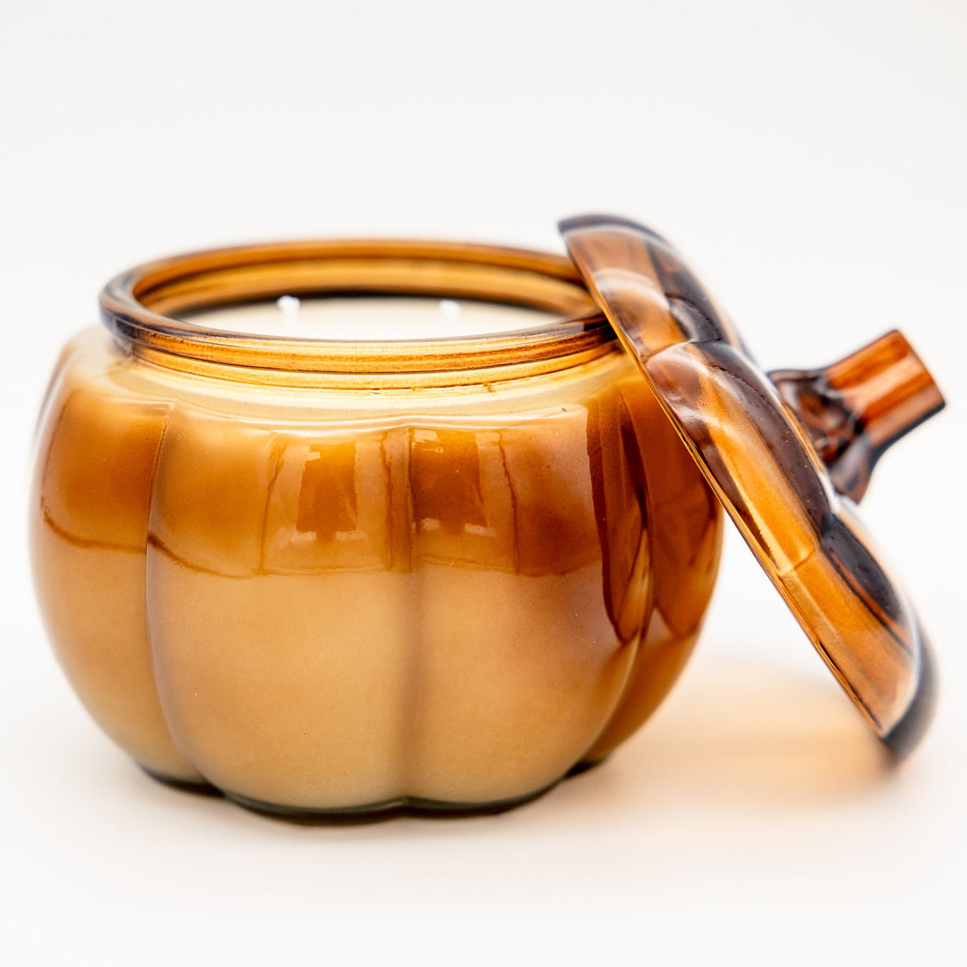 An amber glass pumpkin-shaped jar with a matching lid leaning against it, photographed on a clean white background.