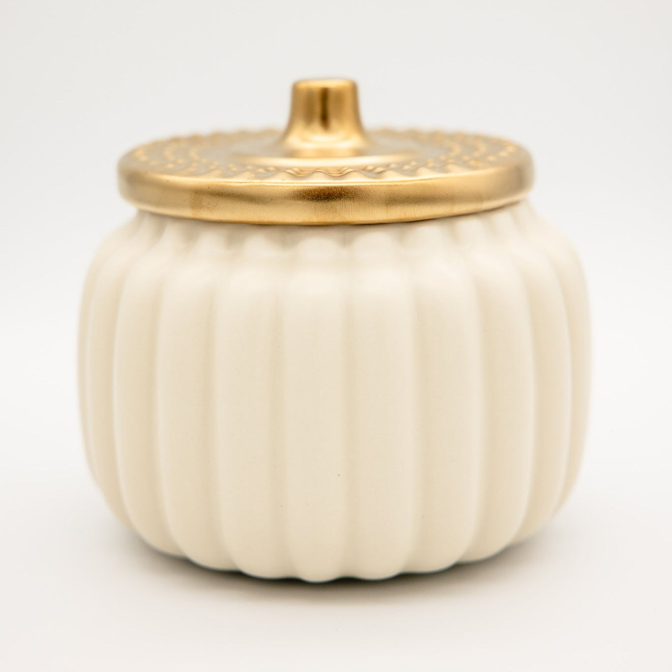 
                  
                    An off-white ribbed ceramic pumpkin-shaped container with a matching lid featuring a gold-toned handle and decorative gold trim, set against a plain white background.
                  
                