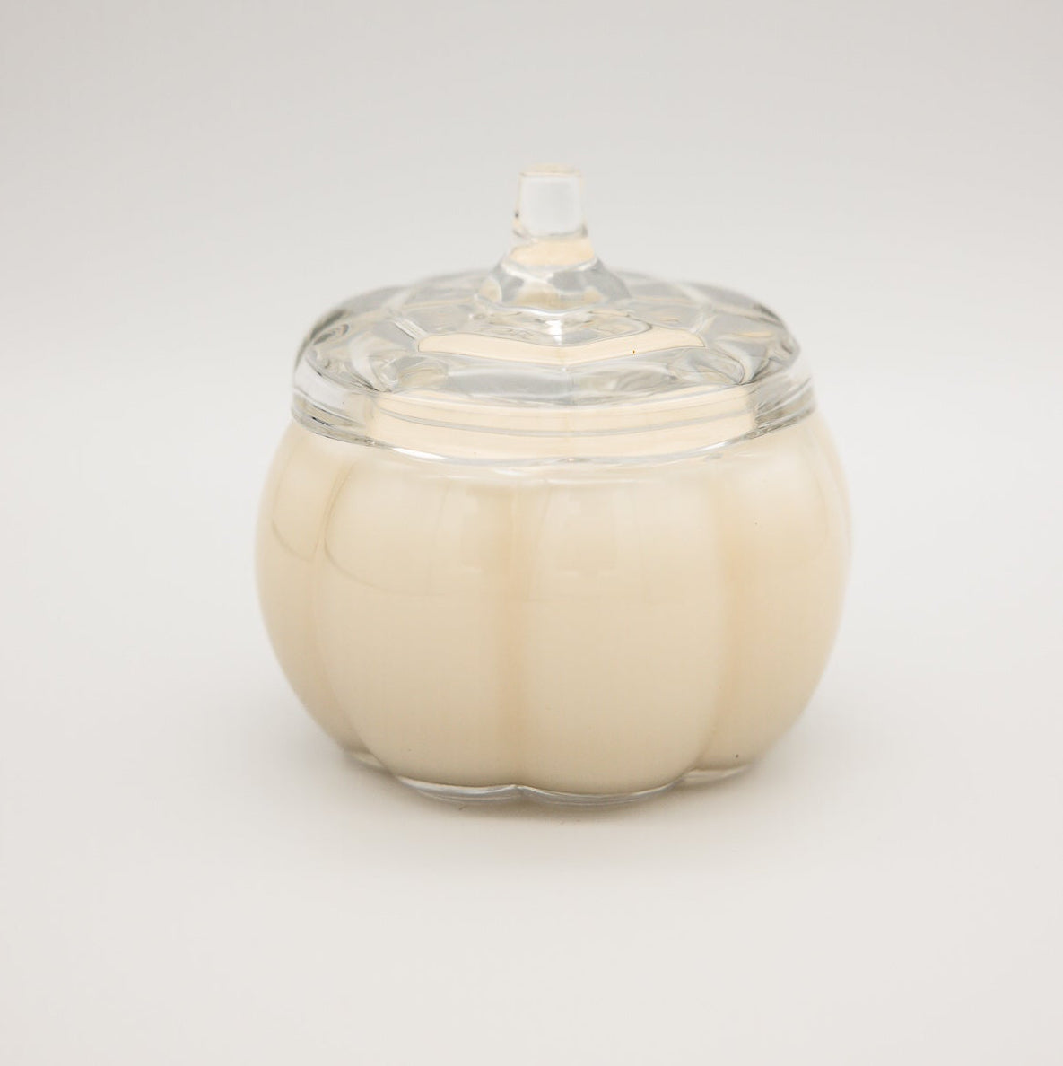 
                  
                    A cream-colored candle in a ribbed glass pumpkin-shaped jar with a matching clear glass lid, set against a seamless light gray background.
                  
                