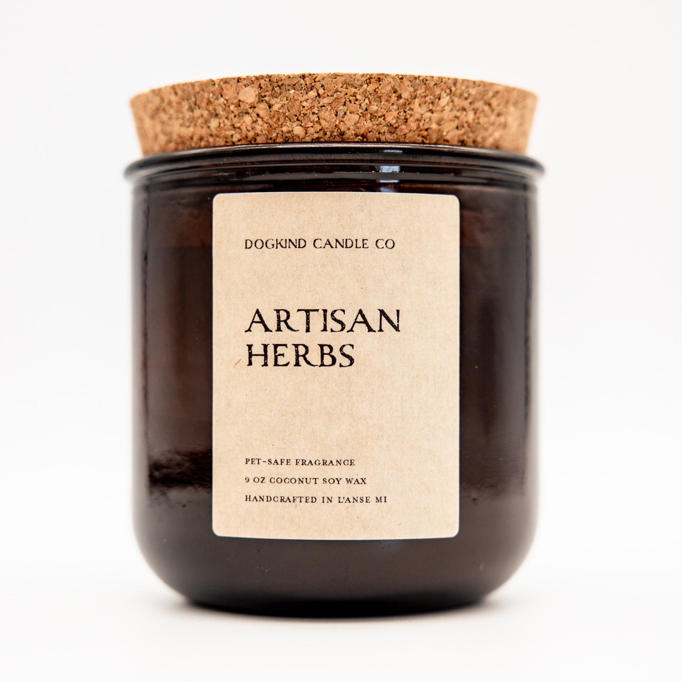 A dark amber glass jar candle with a natural cork lid and a cream paper label reading 'Dogkind Candle Co. Artisan Herbs' on a white background.
