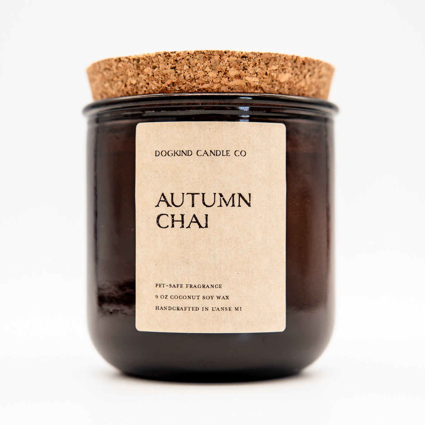 A dark amber glass jar candle with a natural cork lid and a cream paper label reading 'DOGIND CANDLE CO. AUTUMN CHAI' on a clean white background.