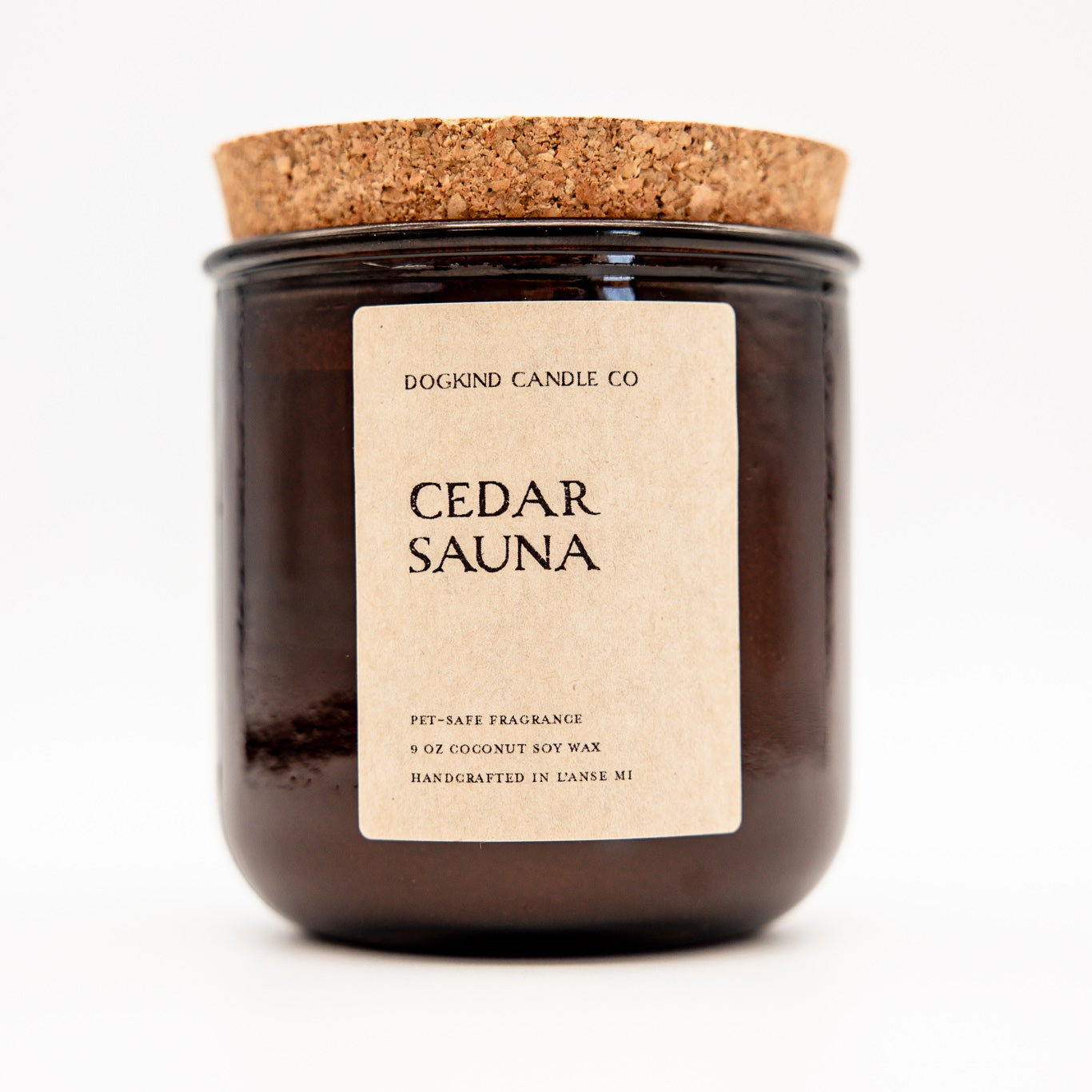 A dark amber glass jar candle with a cork lid and a beige paper label reading 'CEDAR SAUNA' and 'DOGKIND CANDLE CO', photographed on a clean white background.