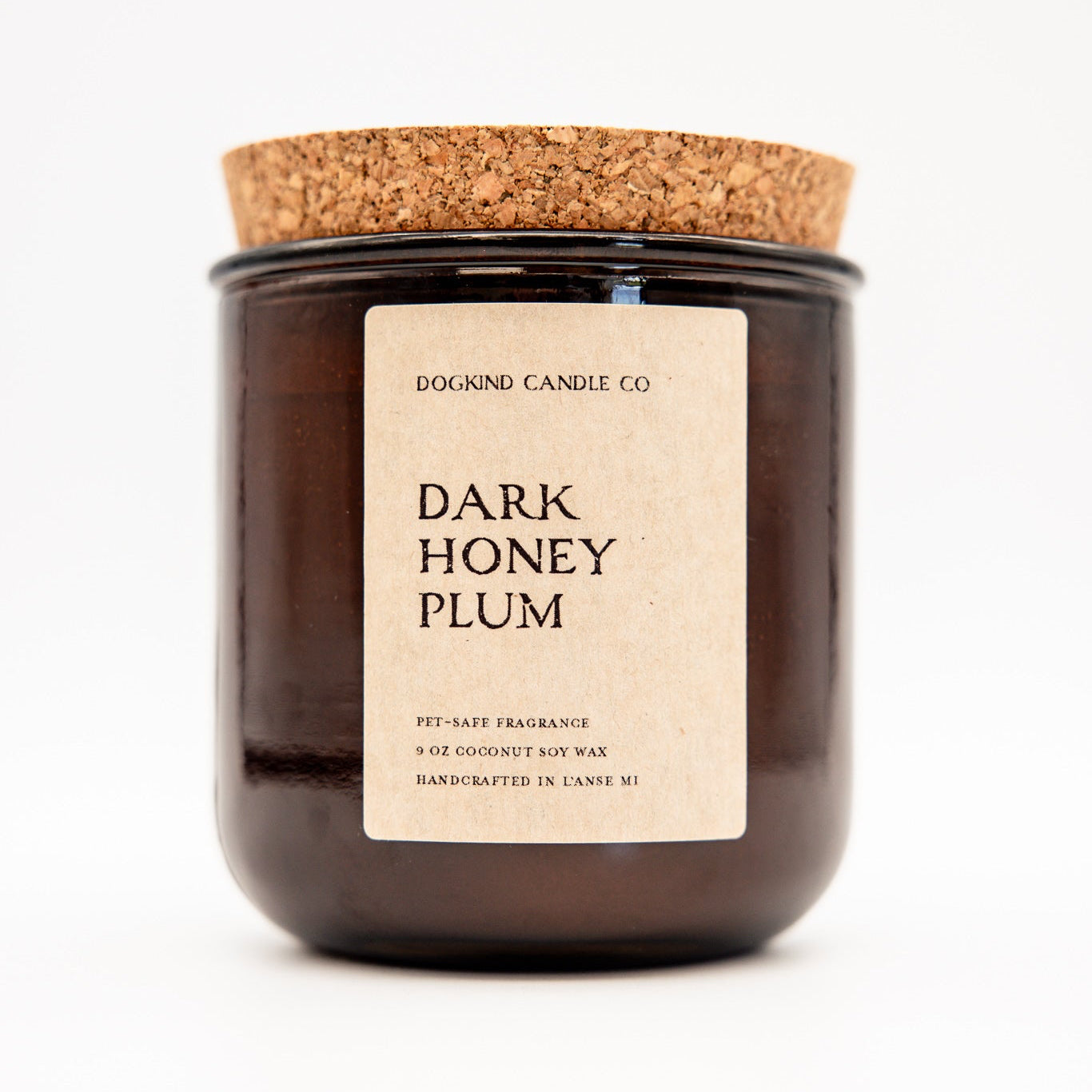A dark amber glass jar candle with a cork lid and a cream paper label reading 'DOGKIND CANDLE CO. DARK HONEY PLUM'.