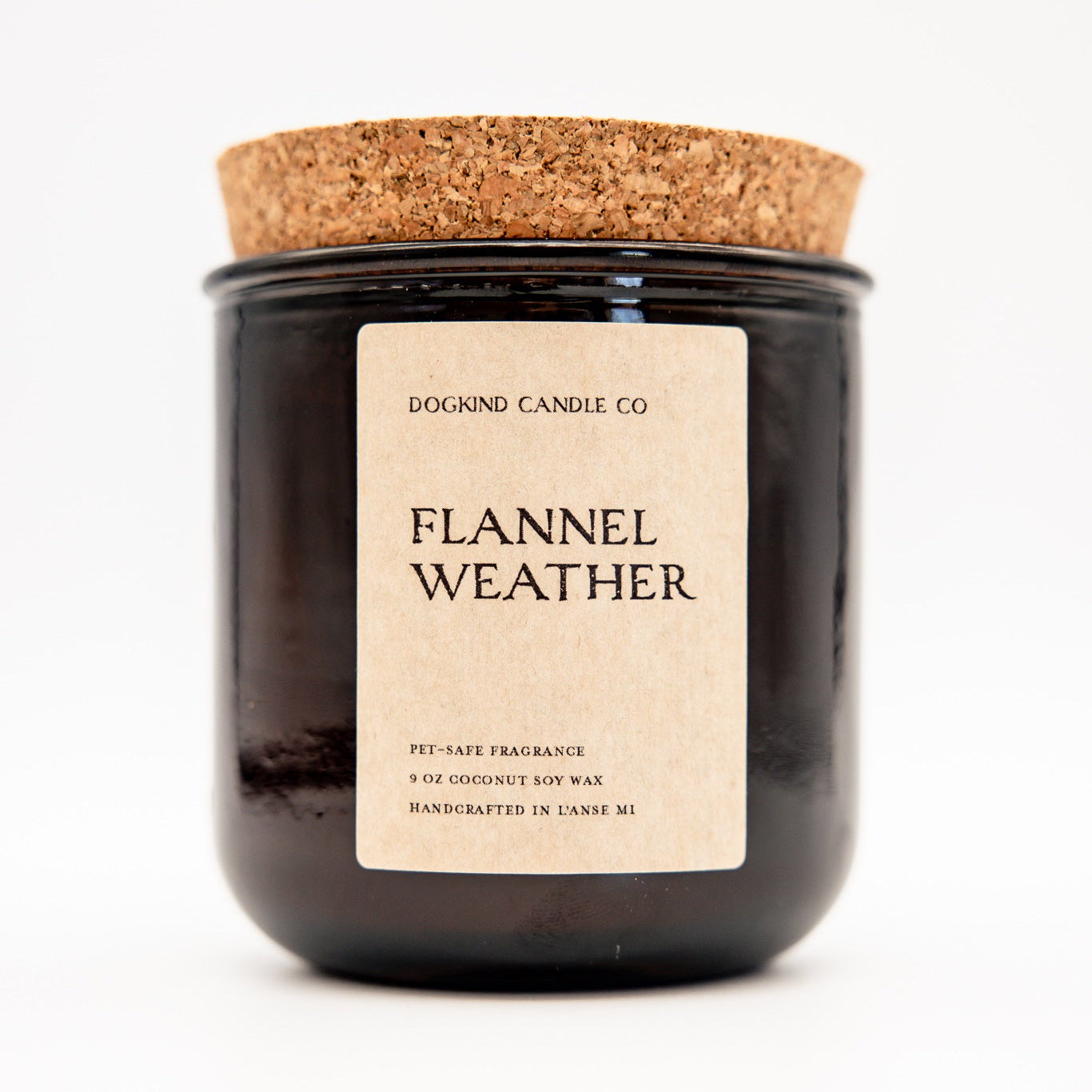 A dark glass jar candle with a cork lid and a cream paper label reading 'DOGKIND CANDLE CO. FLANNEL WEATHER'.