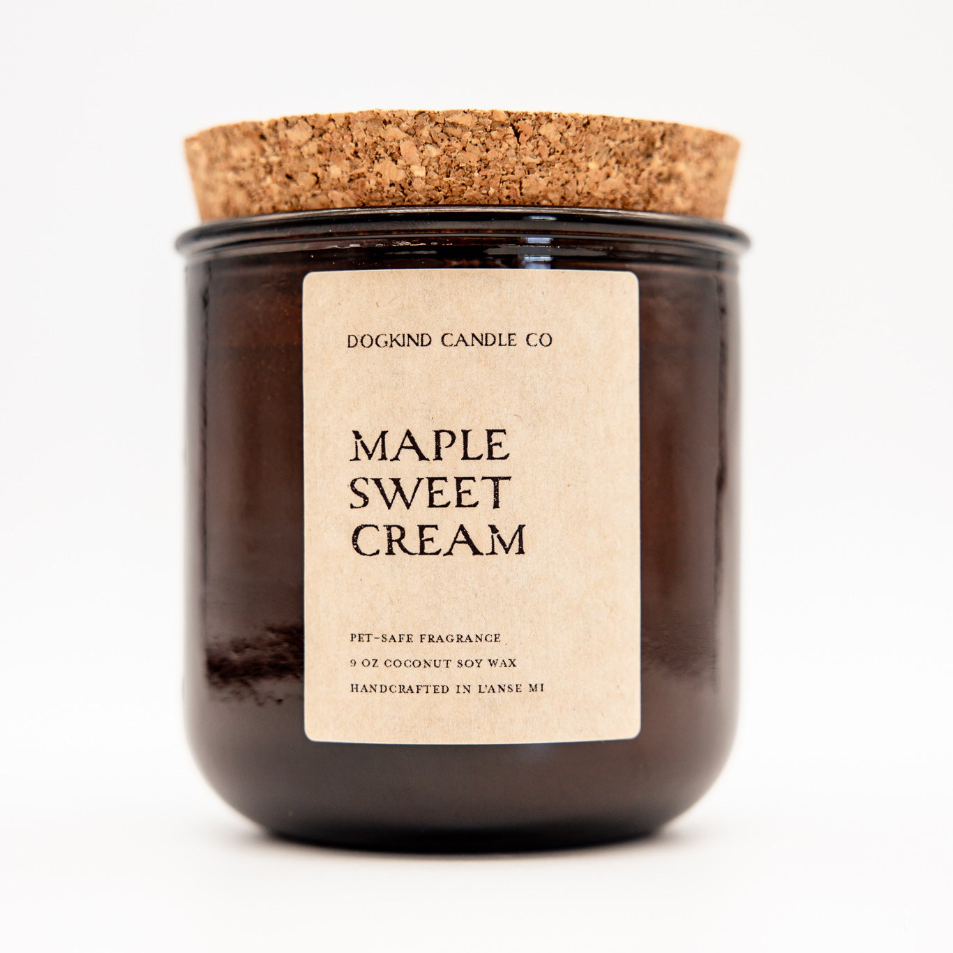 A dark amber glass jar candle with a natural cork lid and a beige paper label reading 'DOGKIND CANDLE CO. MAPLE SWEET CREAM'.