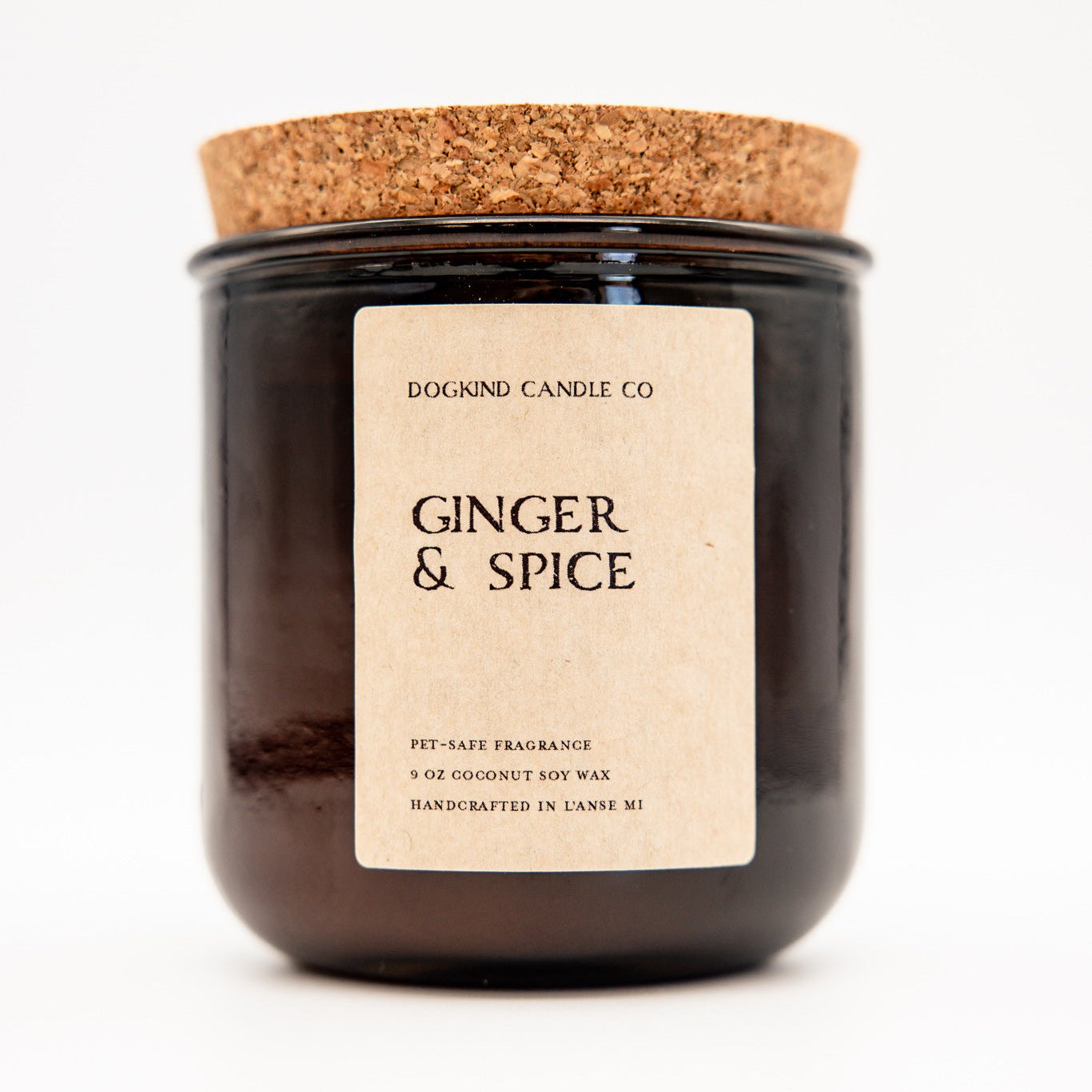 A dark amber glass jar candle with a natural cork lid and a cream paper label reading 'DOGKIND CANDLE CO' and 'GINGER & SPICE'.