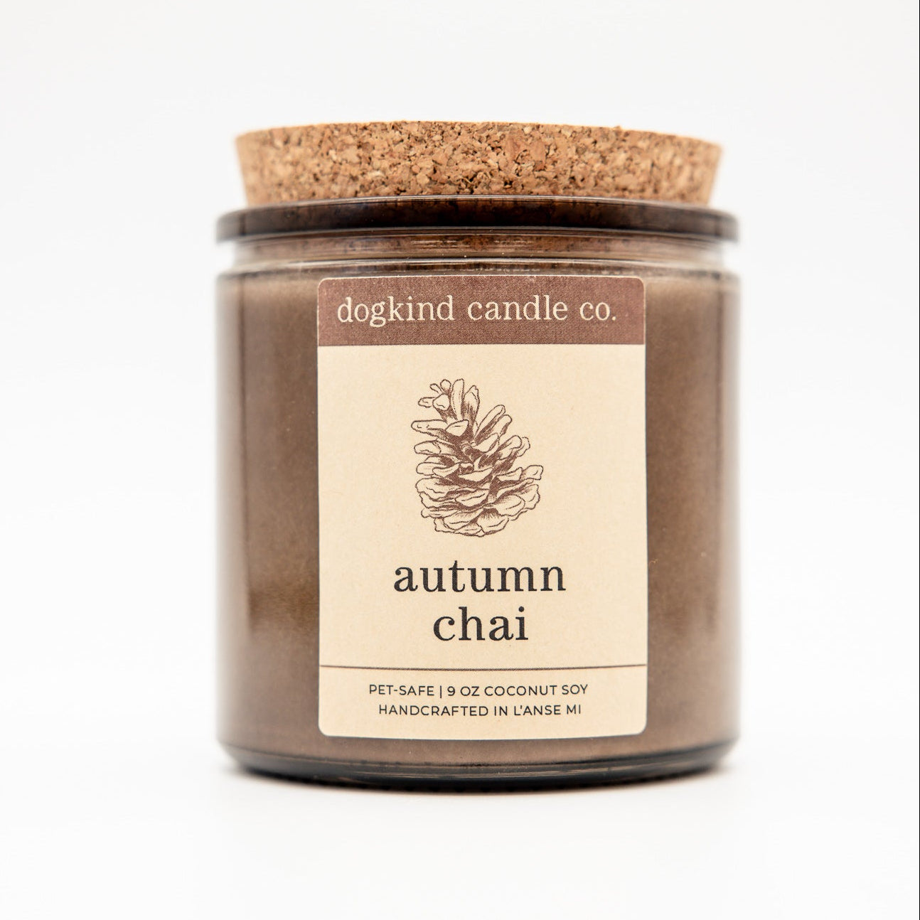 A jar candle from dogkind candle co. labeled 'autumn chai' with a cork lid and a cream label, shown on a plain white background.