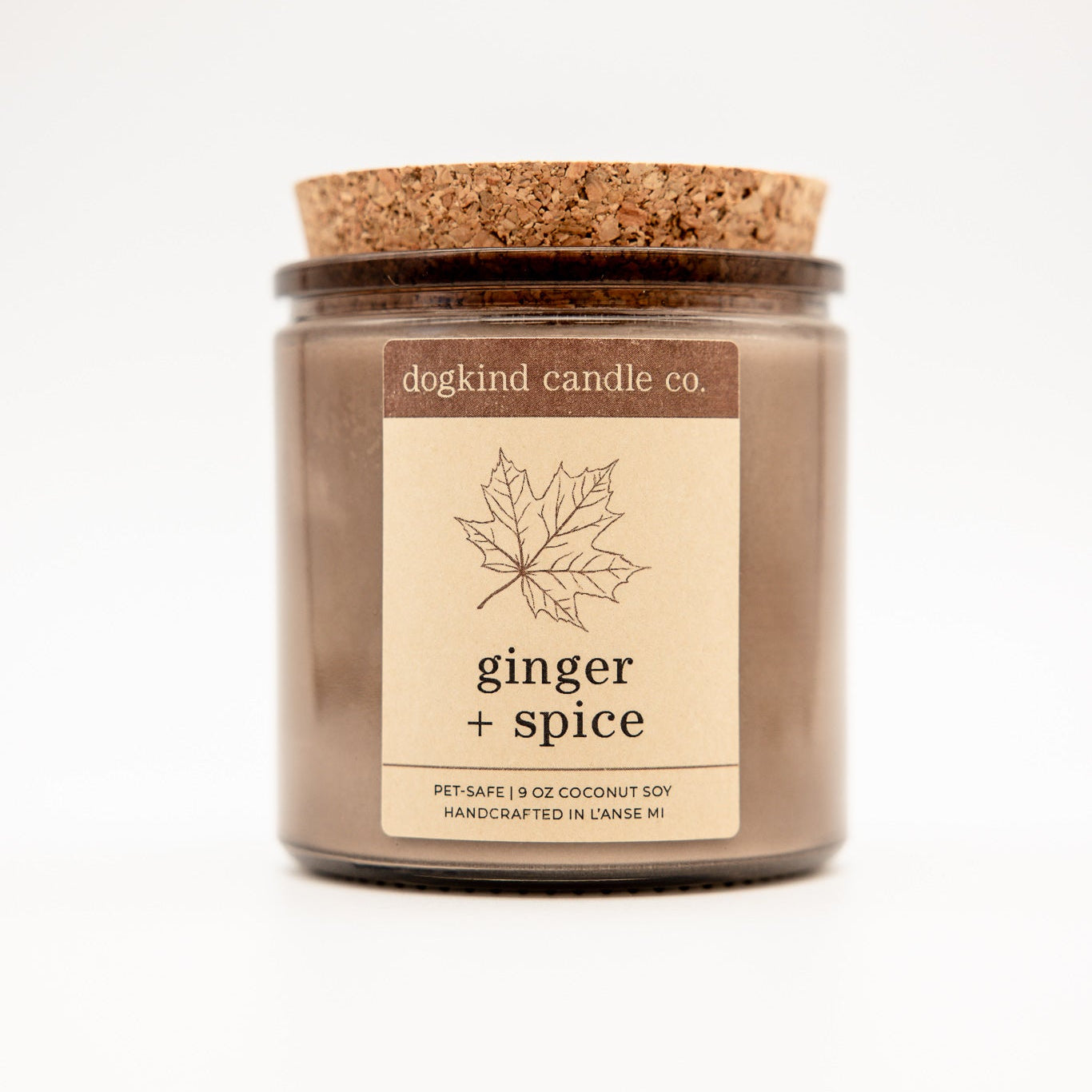 A large coconut soy candle in a clear glass jar with a brown wax fill, a cork lid, and a cream label that reads 'dogkind candle co. ginger + spice'.