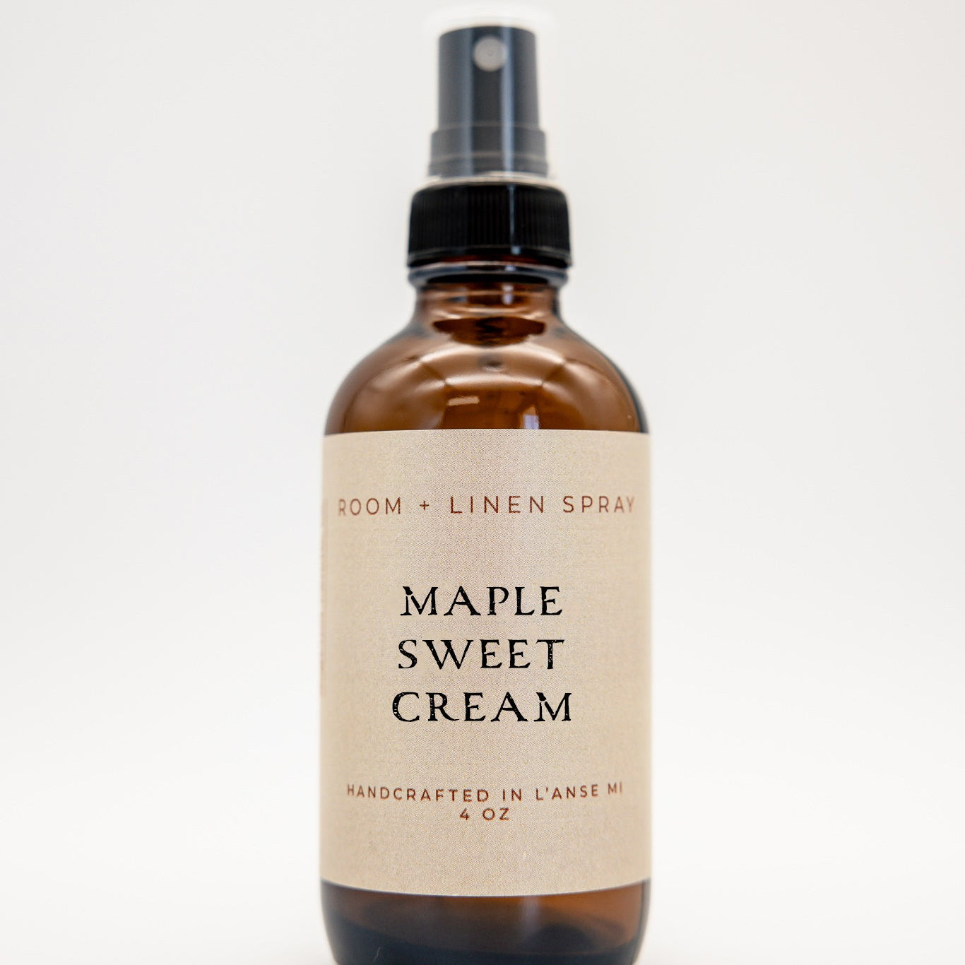 An amber glass spray bottle of Maple Sweet Cream room and linen spray with a black spray nozzle and a beige label, set against a plain white background.